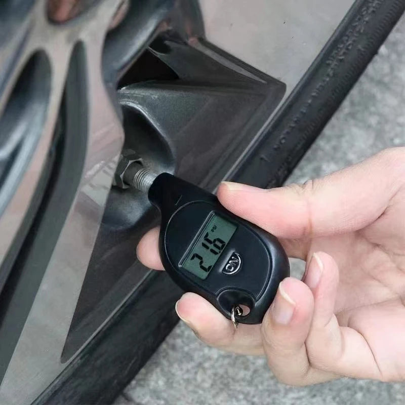 Hand pressing the digital tire gauge onto a car tire valve to read the pressure